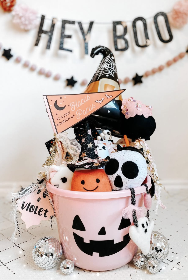 Pink jack-o’-lantern boo basket for kids filled with Halloween plush toys, a Hocus Pocus flag, and festive decorations.