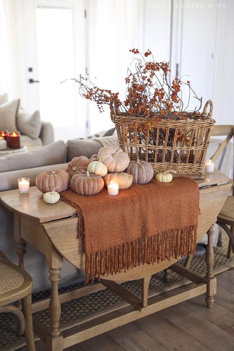 Farmhouse tabletop decorated with velvet pumpkins, a burnt orange throw, wicker basket of berries, and glowing candles.