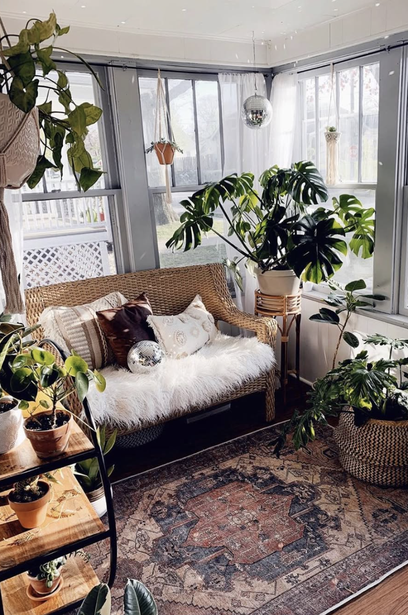 Sunlit reading nook in a sunroom with rattan loveseat, fluffy white cushion, disco ball, and lush green plants