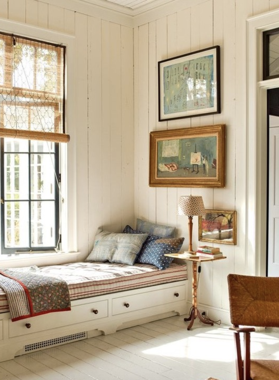 Charming vintage-style reading nook with beadboard walls, striped bench cushion, eclectic pillows, and framed artwork above