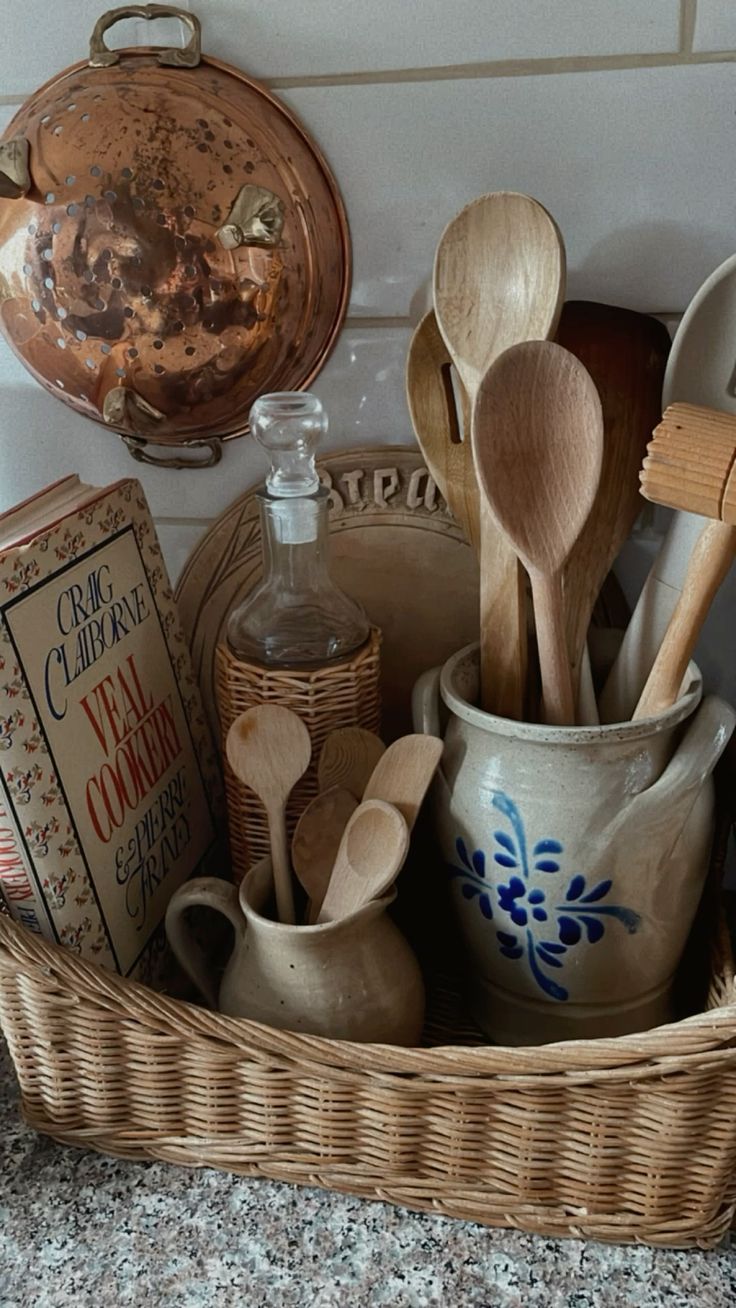 A cozy grandmacore kitchen vignette with a vintage cookbook on display, wooden spoons in a ceramic crock, a wicker basket, and a hanging copper pot, capturing nostalgic kitchen charm.