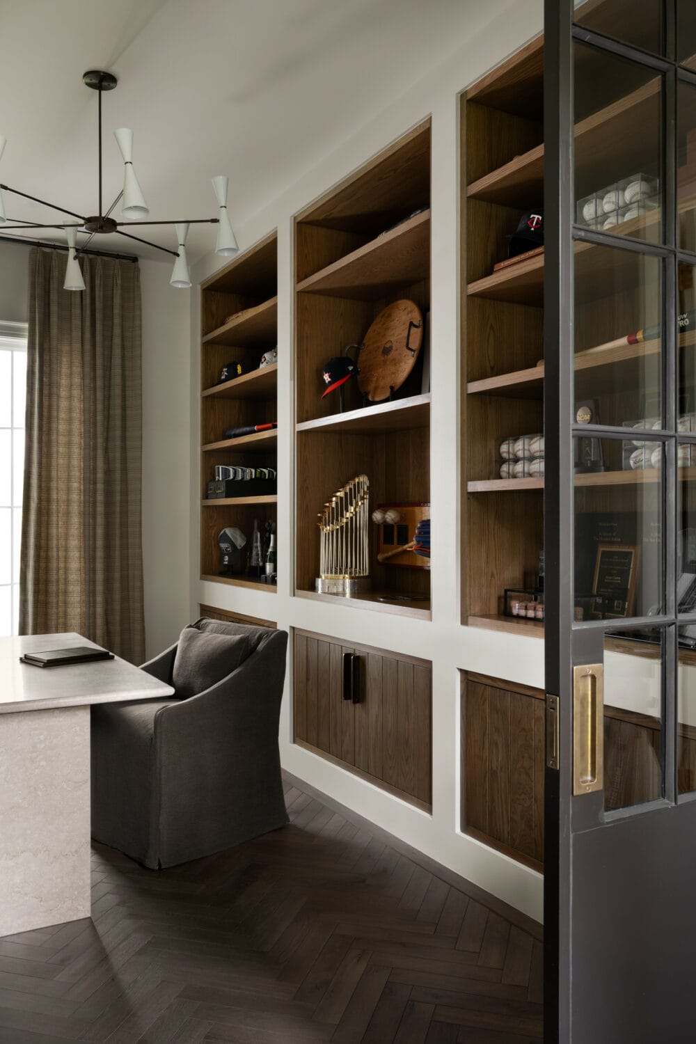 Studio McGee office featuring dark wood built-in shelving, a modern chandelier, and a stone desk with upholstered chair.