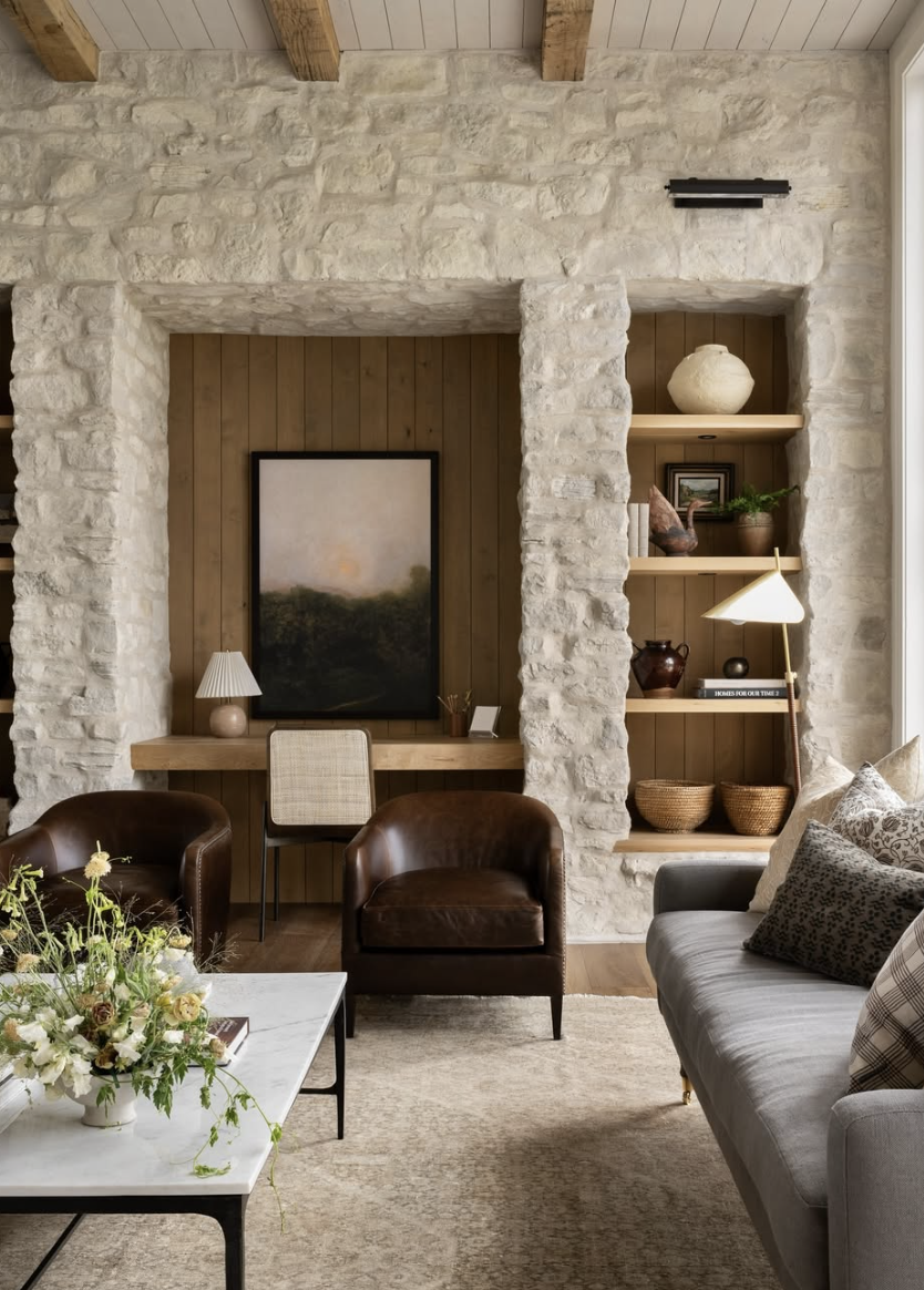 Studio McGee office nook framed by stone walls with wood paneling, a floating desk, and built-in shelving styled with pottery and books.