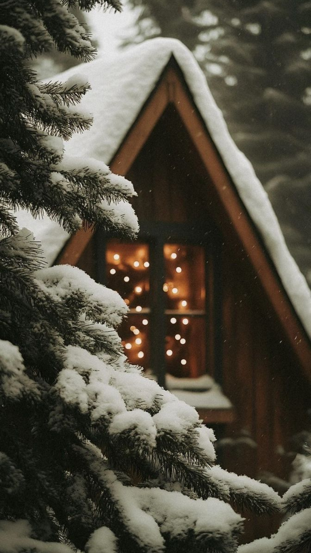 Cozy cabin winter aesthetic wallpaper with snow-covered trees and glowing fairy lights inside a rustic wooden cabin.
