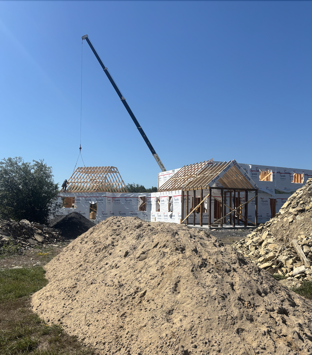Modern farmhouse build in the framing stage with visible window cutouts and Tyvek wrap on the main floor walls.