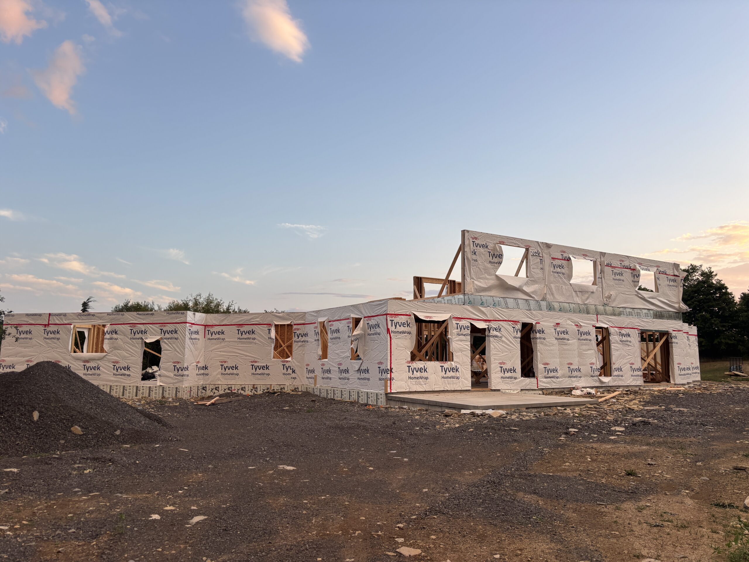 Framing process of a modern farmhouse with Tyvek wrap, showing exterior walls and second-story structure under construction during the house build.