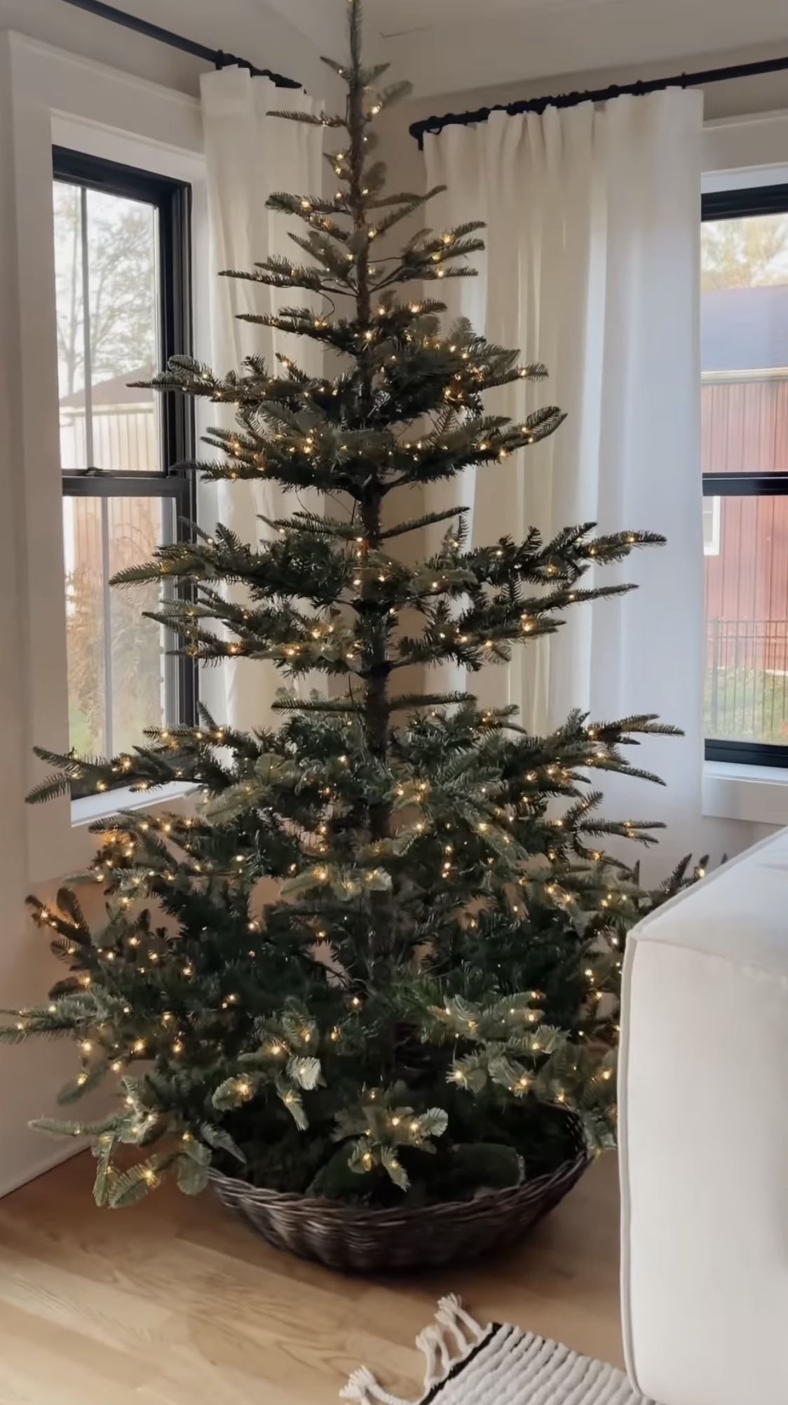 Christmas tree with a low woven basket tree collar and warm white lights for a simple farmhouse Christmas decor look.