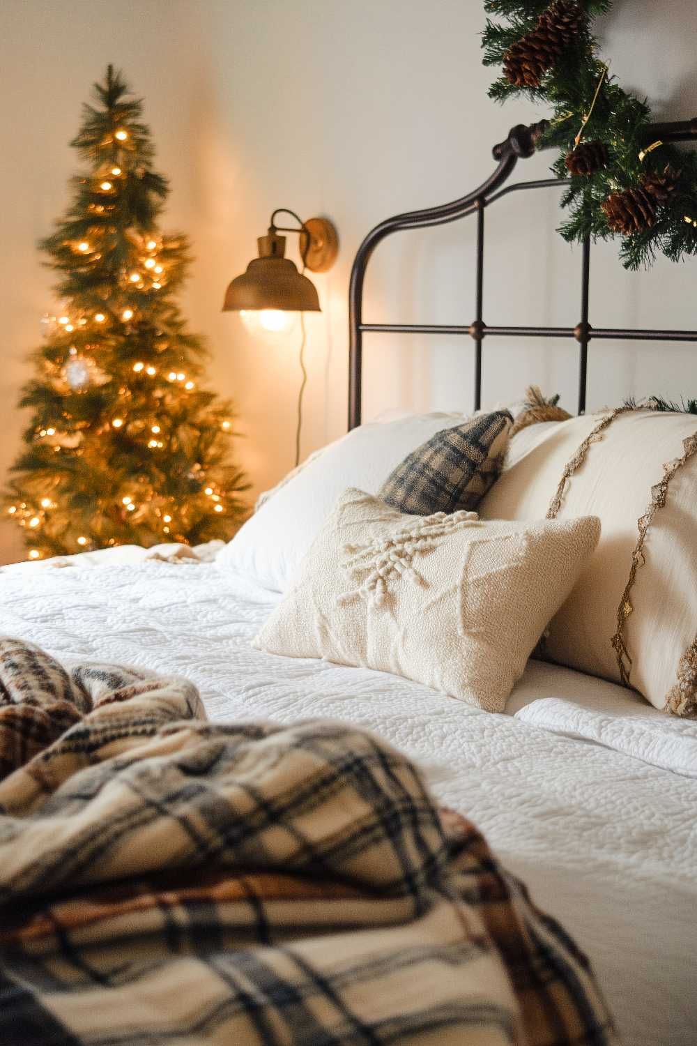 neutral farmhouse christmas bedroom with small lit christmas tree, plaid blanket, and simple greenery on headboard