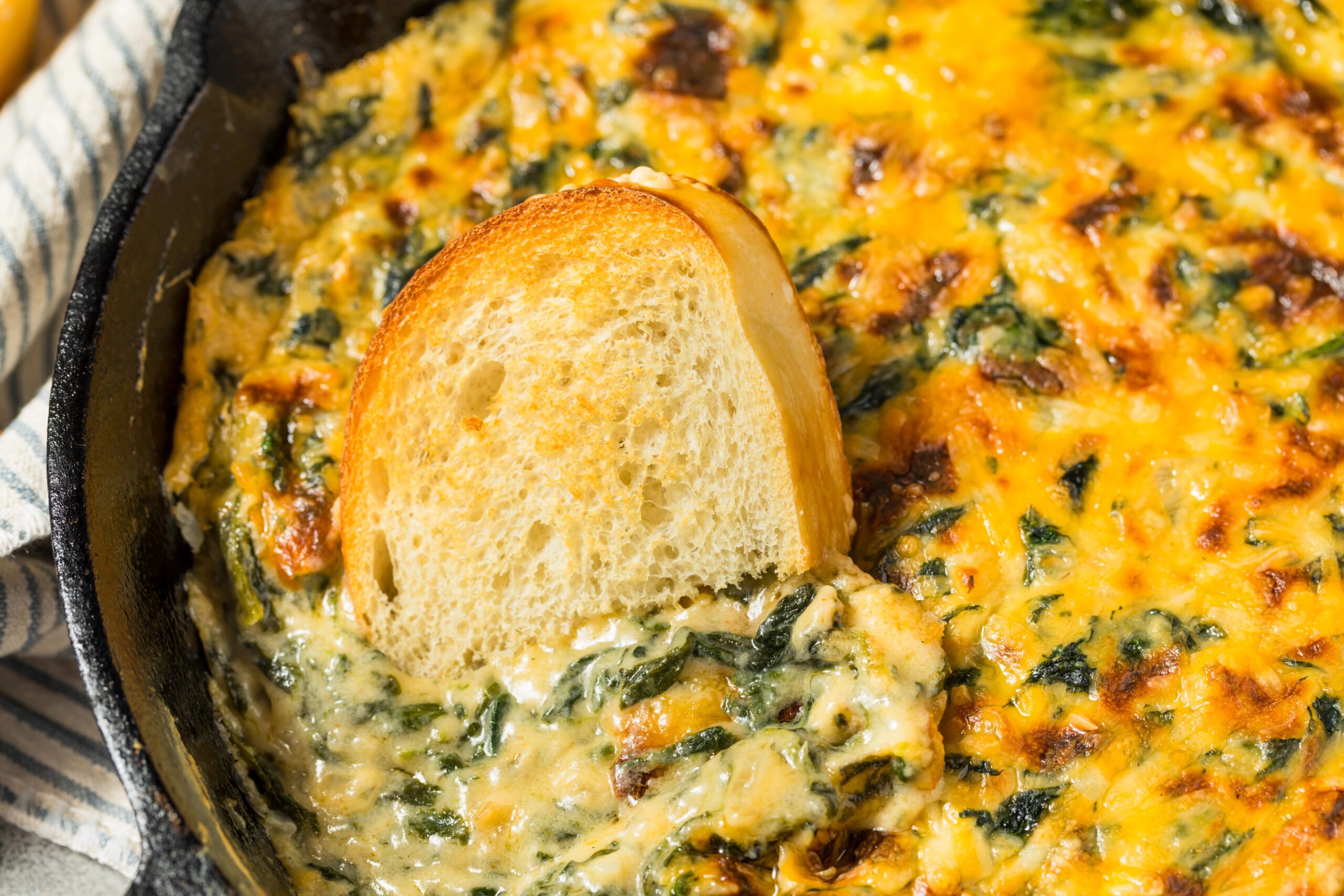 Close-up of cheesy Spinach Maria Dip being scooped with toasted bread, showing gooey melted cheese and creamy spinach filling.