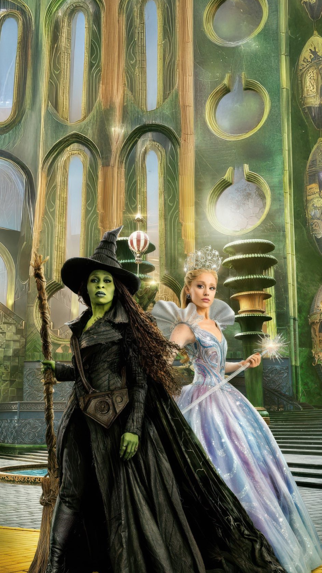 Wicked iPhone wallpaper showing Glinda and Elphaba standing together inside the Emerald City, surrounded by ornate green architecture and magical details.