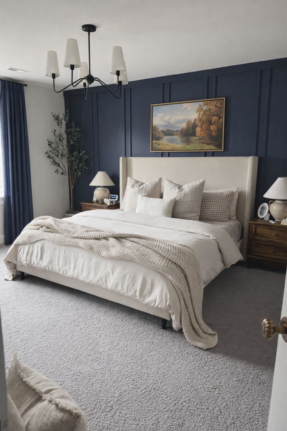 Bedroom with dark blue paneled accent wall, beige upholstered bed, neutral bedding, and framed landscape artwork