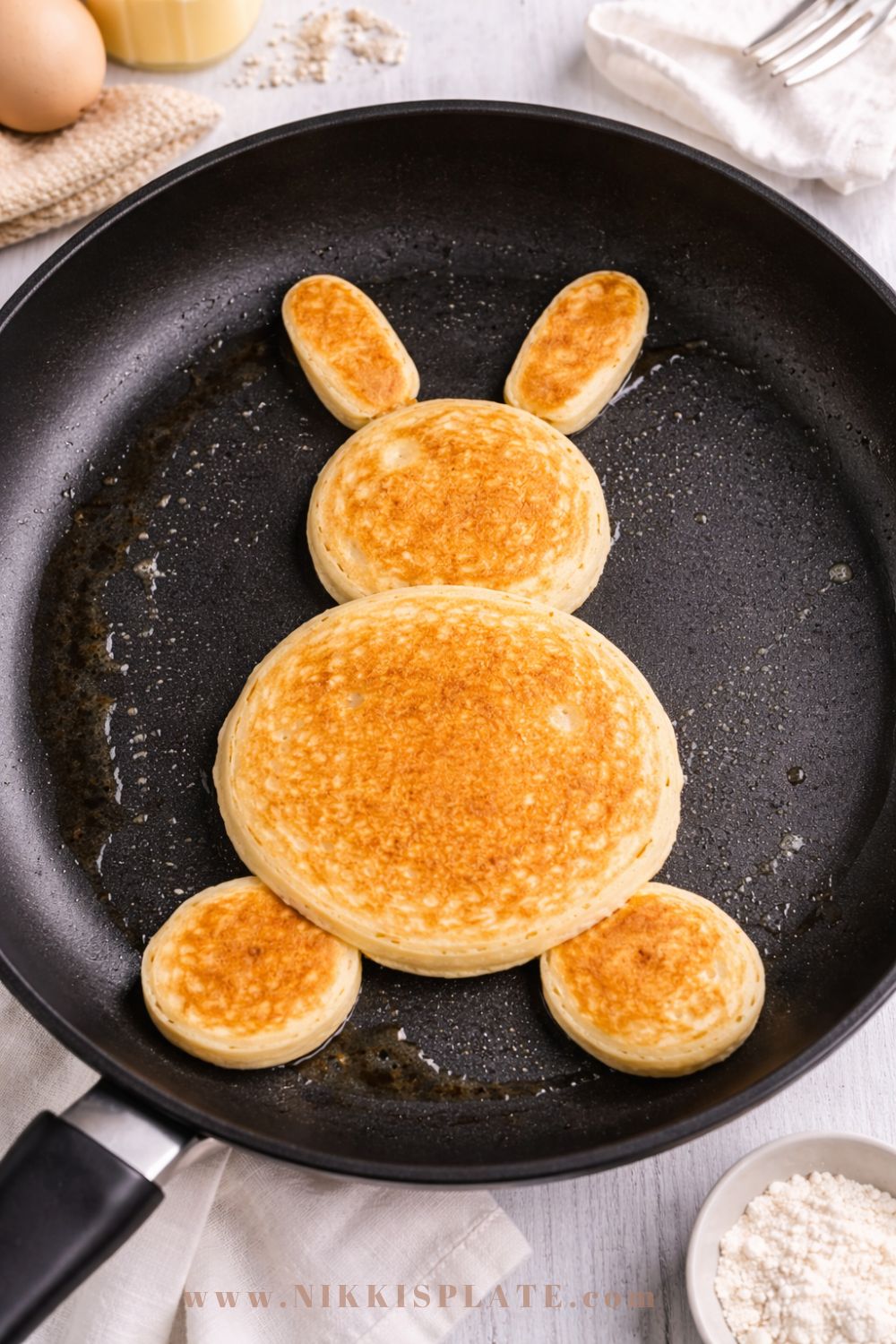 Sourdough Easter bunny pancakes cooking in a skillet shaped into body, head, ears, and feet before decorating