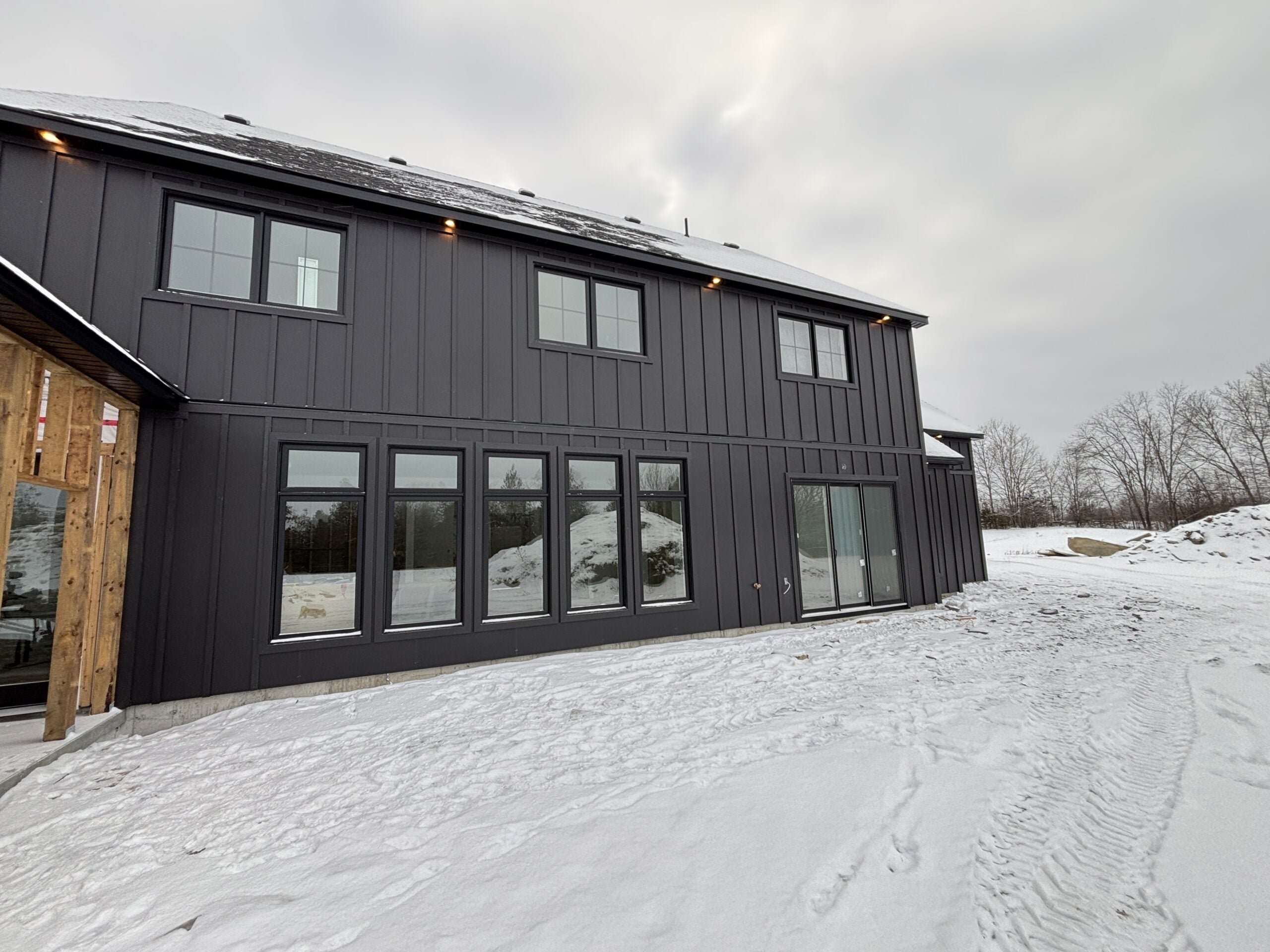 Black exterior windows and sliding patio door installed on our modern farmhouse build, featuring board and batten siding on our rural Ontario property in winter.
