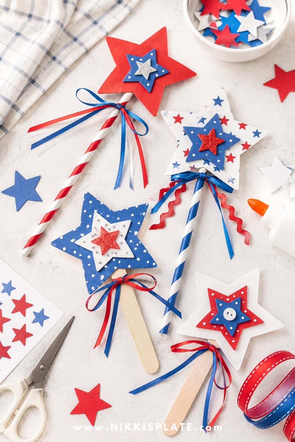 Star wand craft for kids with red, white, and blue paper stars, ribbons, paper straws, and craft supplies on a light table
