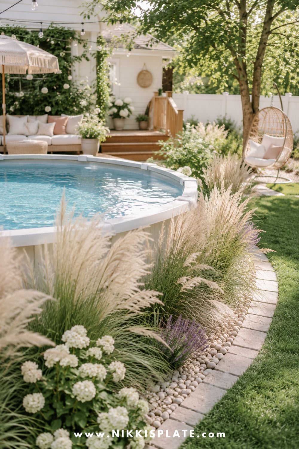 Above ground pool with soft ornamental grasses, white flowers, river rock edging, and a cozy backyard lounge area.