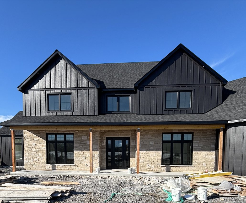 Modern farmhouse exterior with limestone front, black board and batten siding, black windows, and black roof shingles on our rural Ontario custom home build.