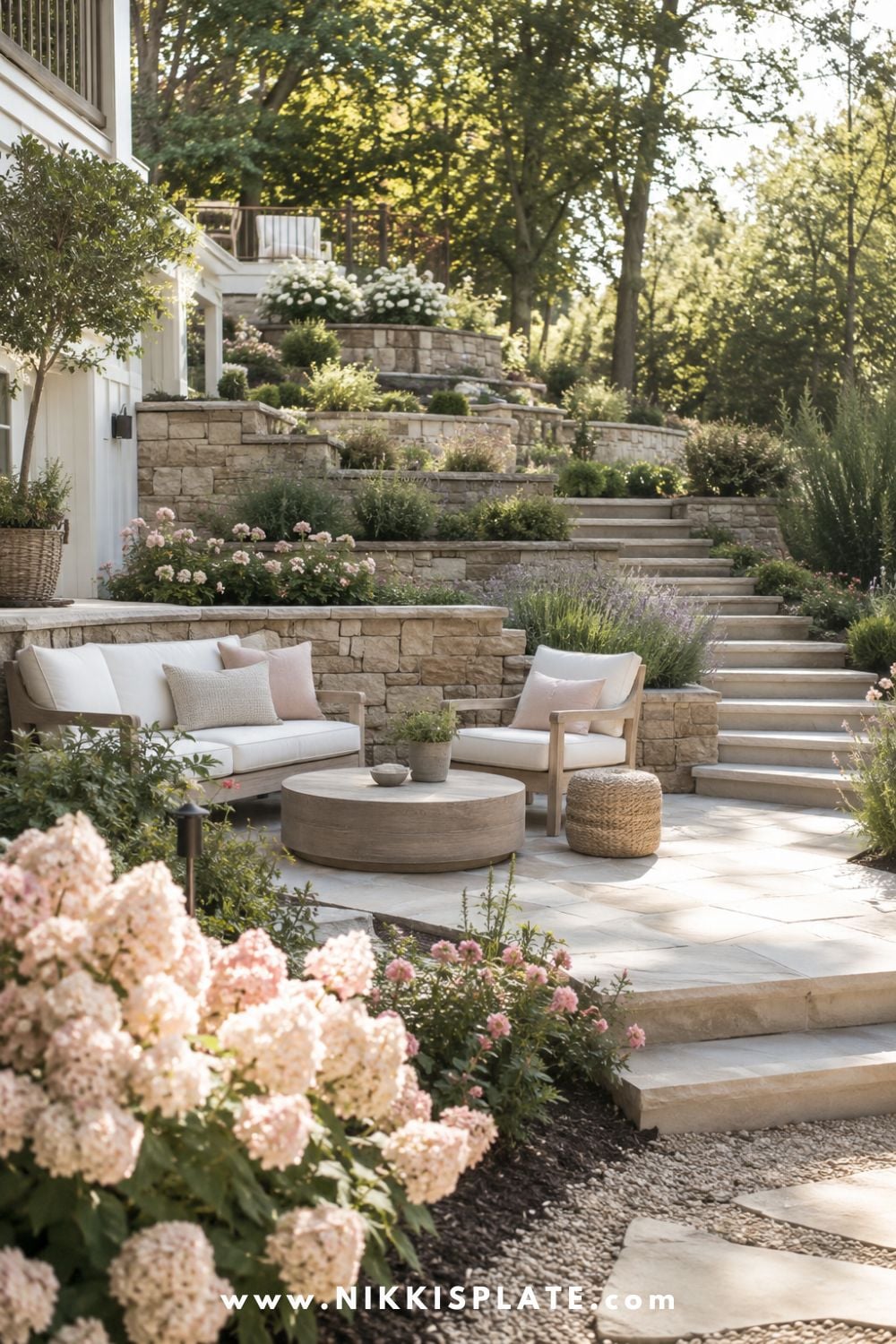 Sloped backyard landscaping with terraced stone walls, cozy patio seating, soft hydrangeas, garden stairs, and layered hillside planting.