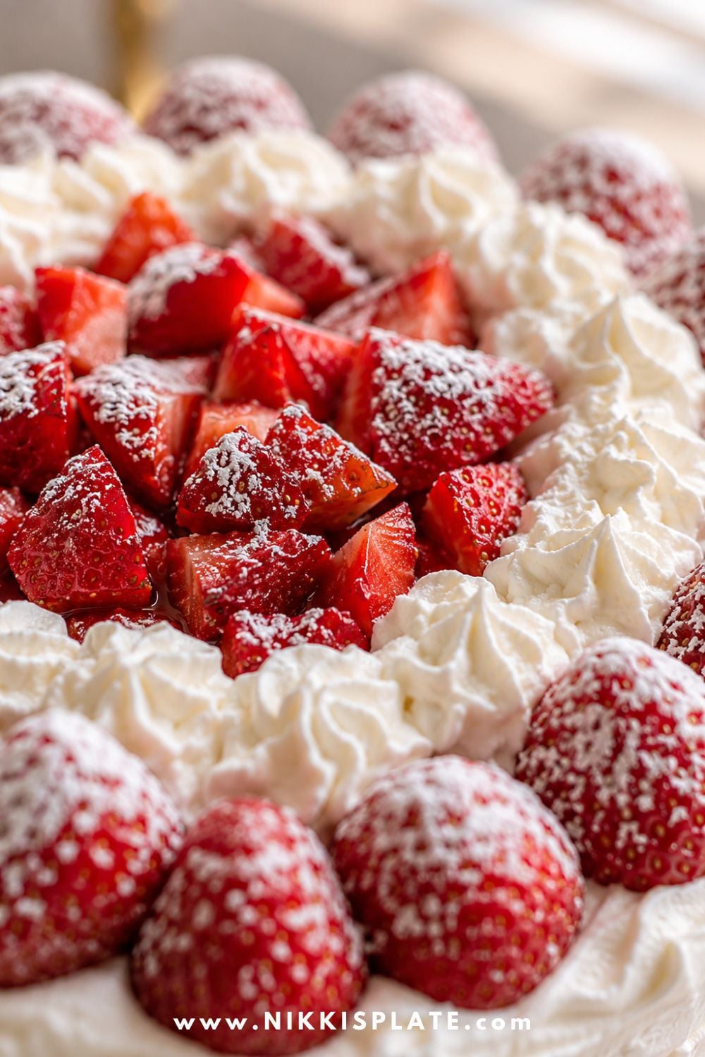 Close-up of homemade strawberry shortcake topped with fresh sliced strawberries, powdered sugar, and piped whipped cream.