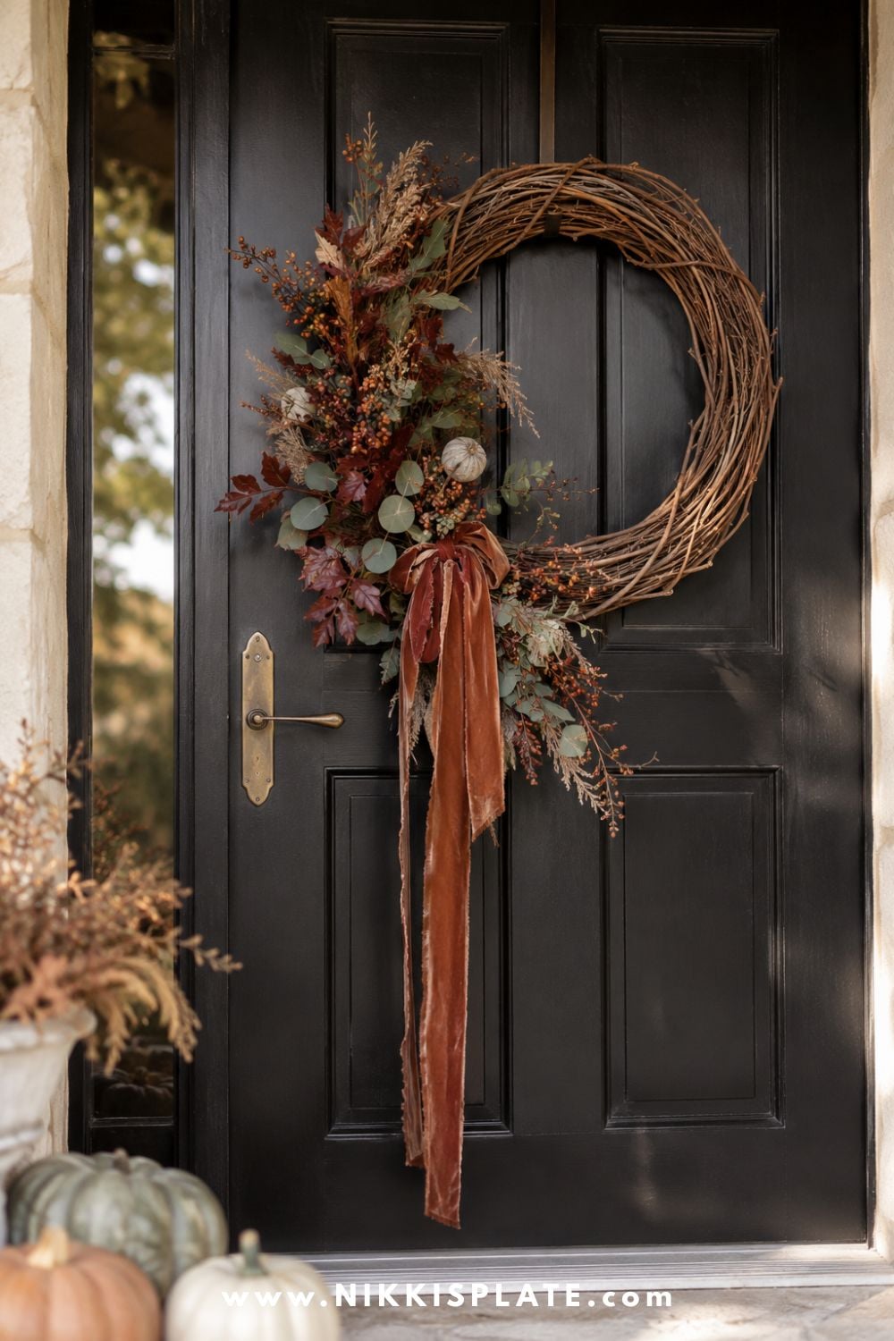 Asymmetrical grapevine fall wreath decorated with burgundy leaves, eucalyptus, berries, dried grasses and a rust velvet ribbon.