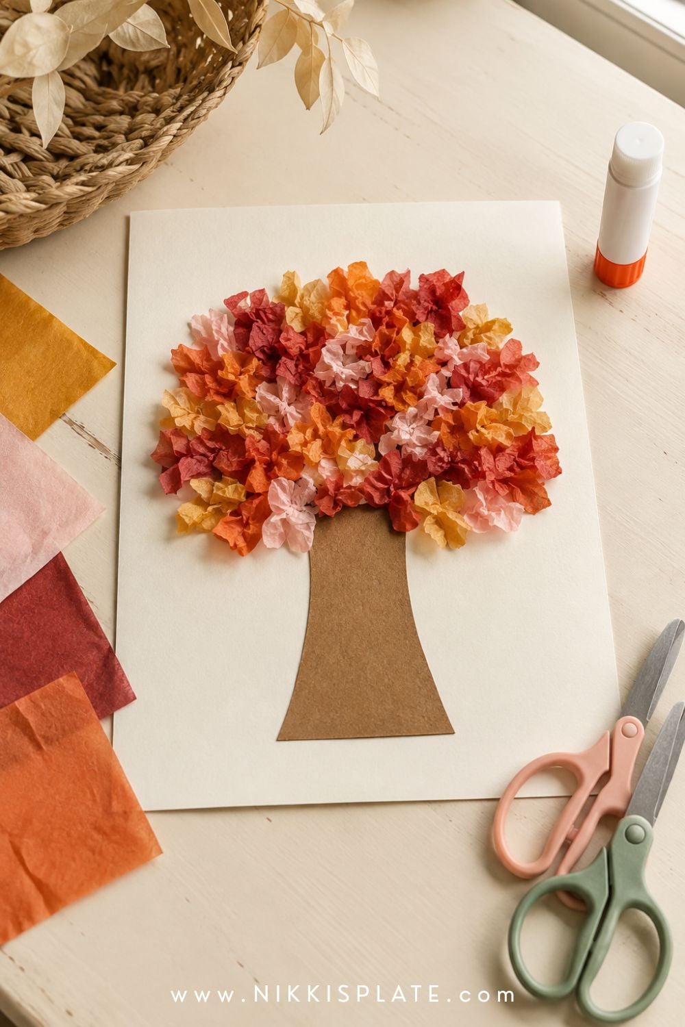 Tissue paper fall tree craft for kids with crumpled red, orange and yellow paper leaves on a brown paper tree.
