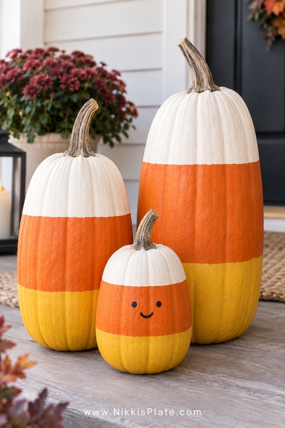 Tall pumpkins painted in white, orange and yellow candy corn stripes.