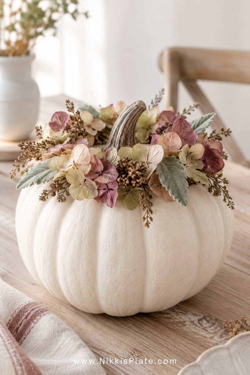 White pumpkin topped with a dried hydrangea and preserved leaf crown.