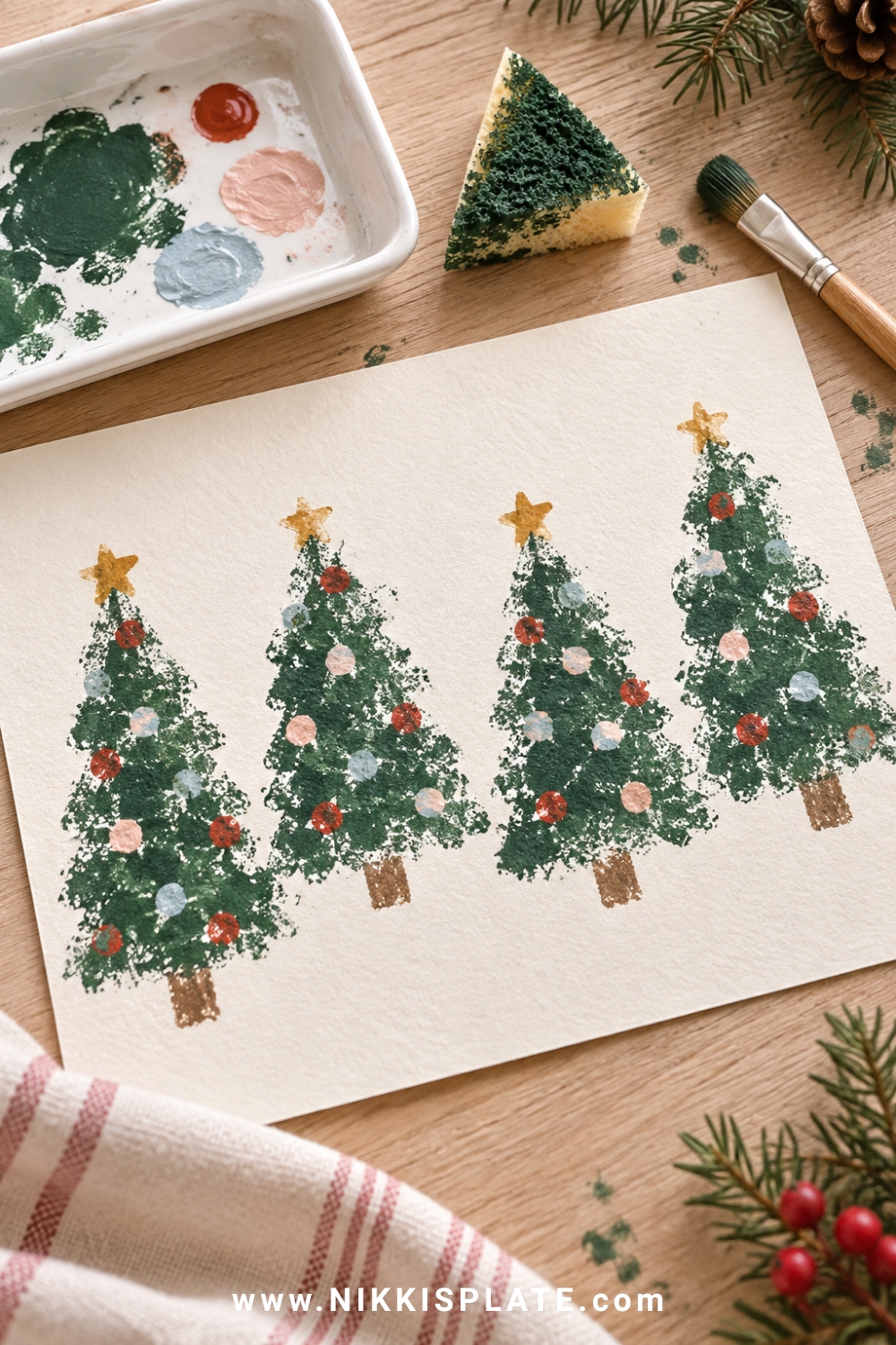 Sponge-stamped green Christmas trees with colourful dotted ornaments, paint tray, sponge and brush.