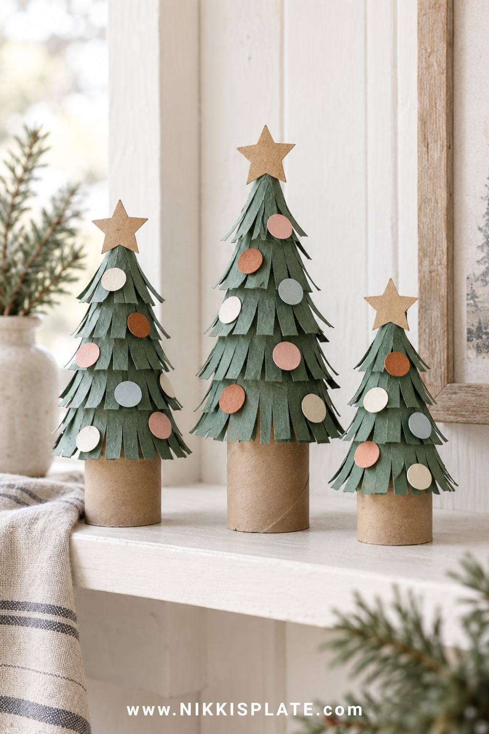 Three cardboard roll Christmas trees with fringed green branches and pastel paper ornaments.