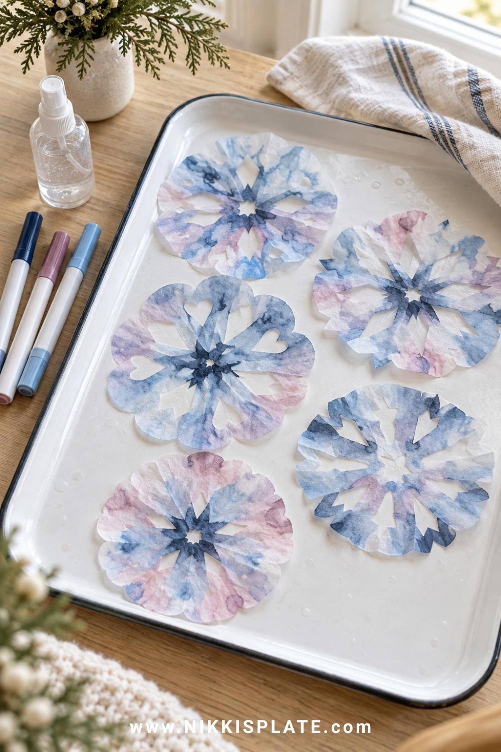 Coffee filter snowflakes with blended blue and mauve colours drying on a white tray.