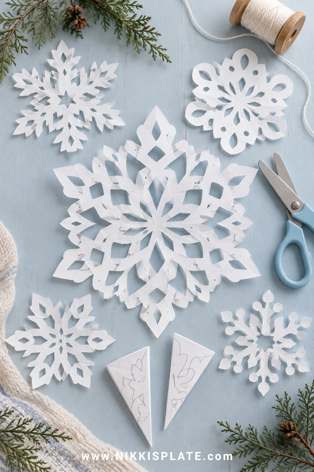 Intricate white paper snowflakes with folded paper wedges and child-safe scissors.