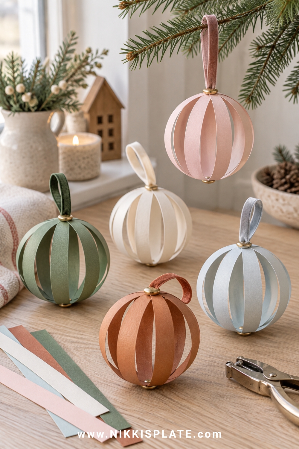 Dimensional paper strip baubles in blush, pale blue, cream, rust and muted green with velvet ribbon loops, arranged beside neatly cut cardstock strips.