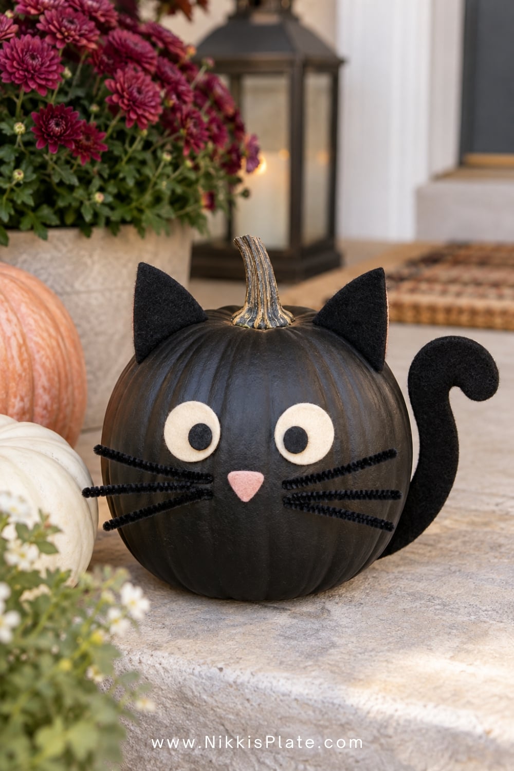 Black pumpkin decorated as a cat with felt ears, eyes, whiskers and tail.