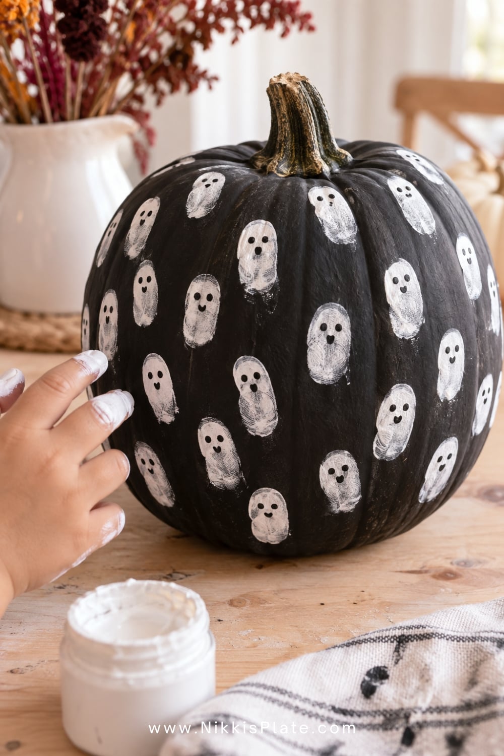 Black pumpkin covered with cute white fingerprint ghosts for a kids Halloween craft.