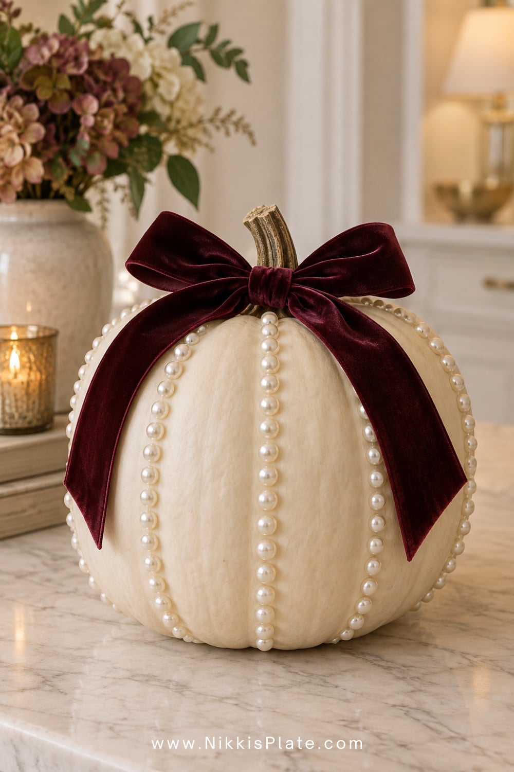 Cream pumpkin decorated with pearl rows and a burgundy velvet bow.