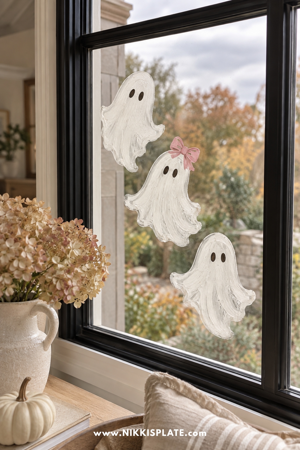 Three white ghosts, one with a blush bow, painted diagonally on glass.