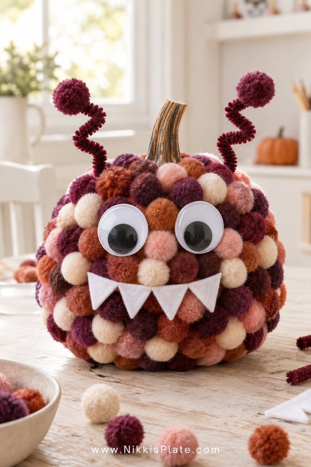 Colourful pom-pom monster pumpkin with big eyes, felt teeth and antennae.