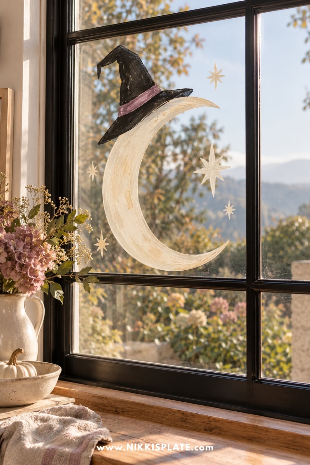 Cream crescent moon painted on glass with a black witch hat and small stars.