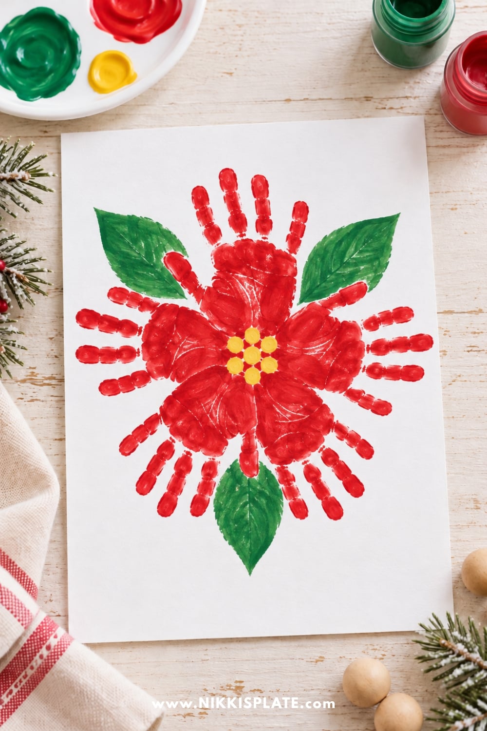 Christmas poinsettia craft made with overlapping red handprints, yellow fingerprint dots, and green leaves on white paper.