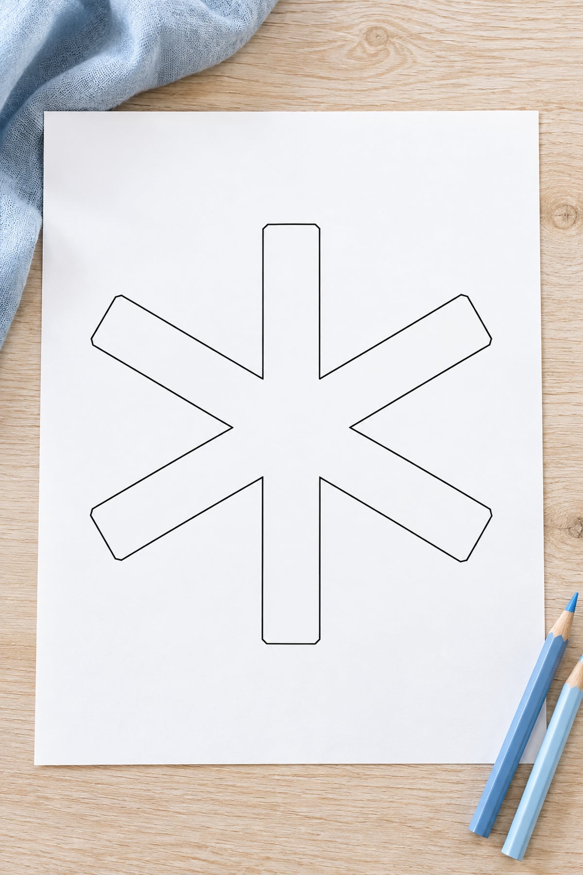 Broad-arm snowflake outline printed on white paper beside two pale blue pencil crayons.