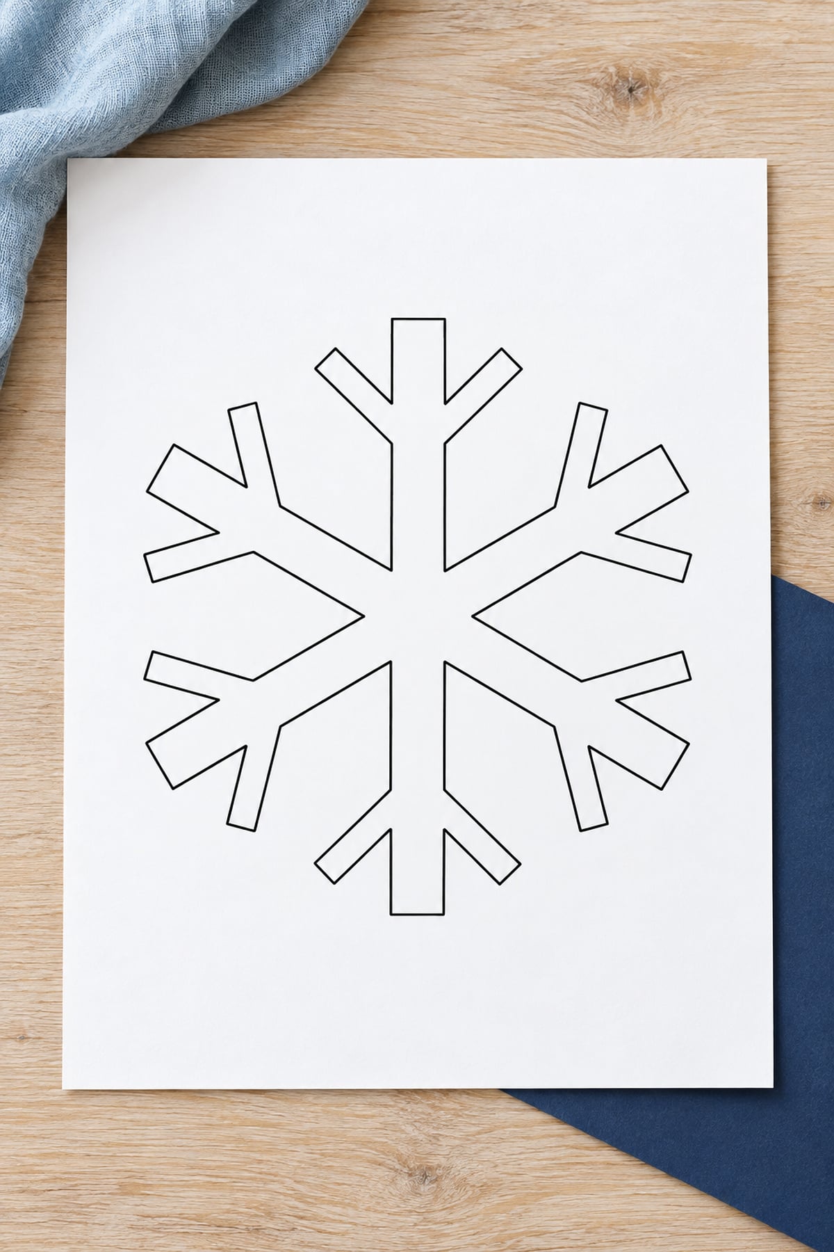 Snowflake template with long side branches on white paper layered over navy paper.