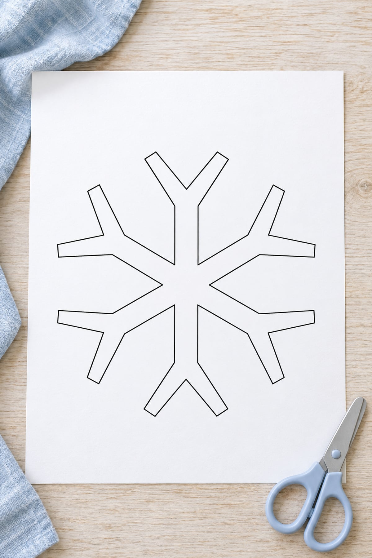 Snowflake template with six forked arms on white paper beside pale blue scissors.