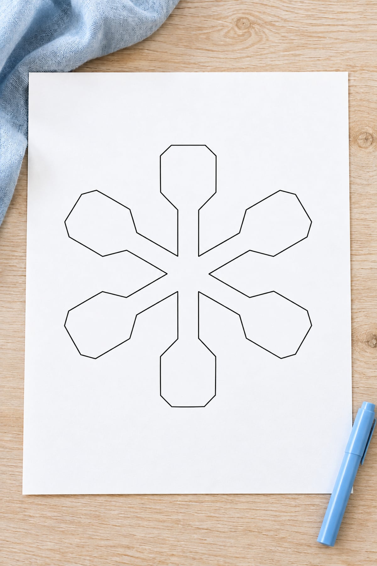 Paddle-tip snowflake outline printed on white paper on a light oak craft table.