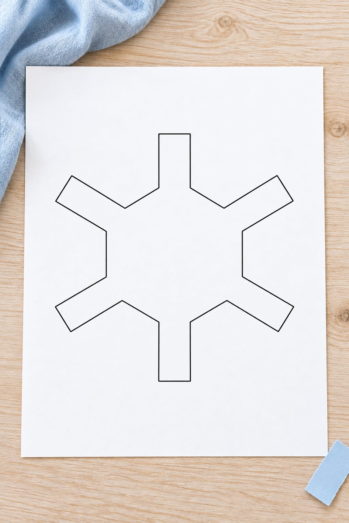 Snowflake template with a large hexagon centre and six short arms beside pale blue paper.