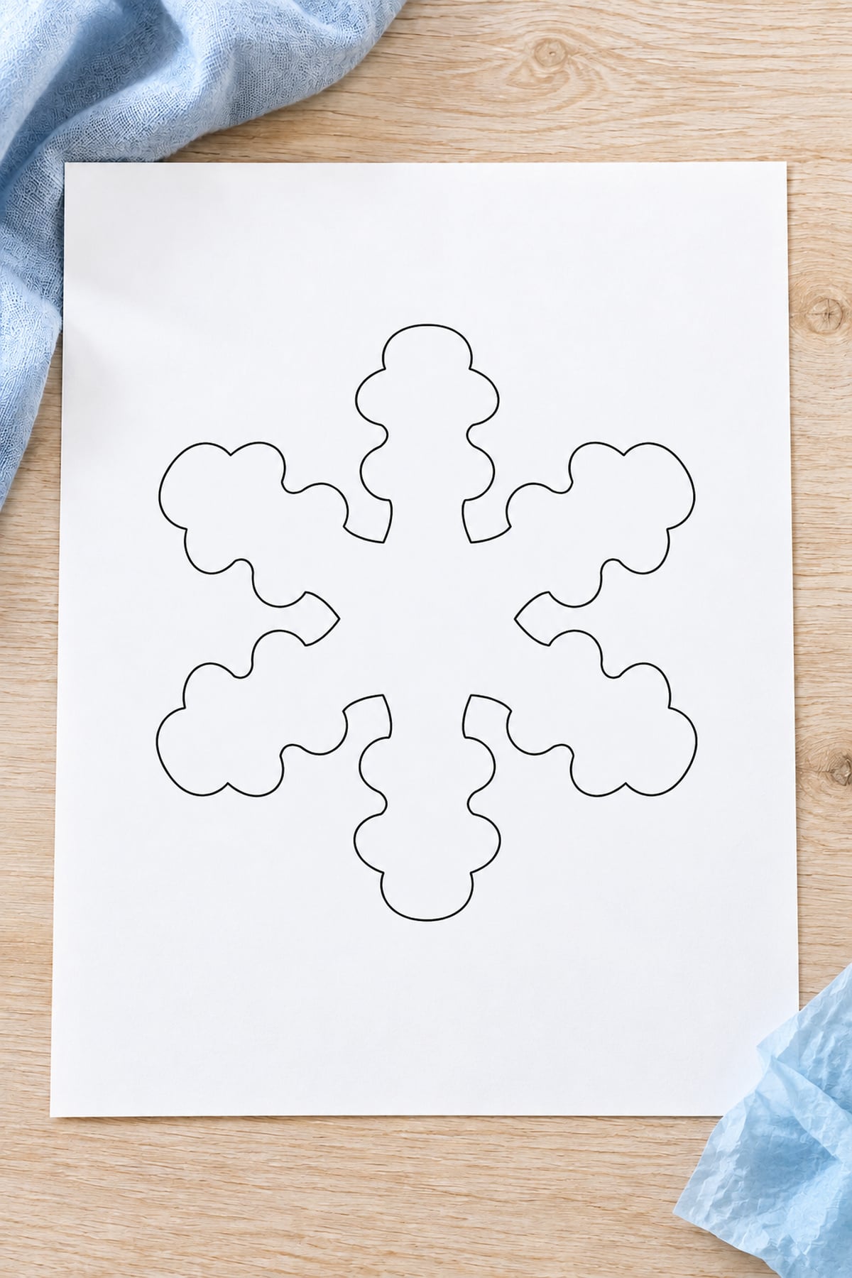 Scalloped snowflake outline on white paper beside pale blue tissue paper.