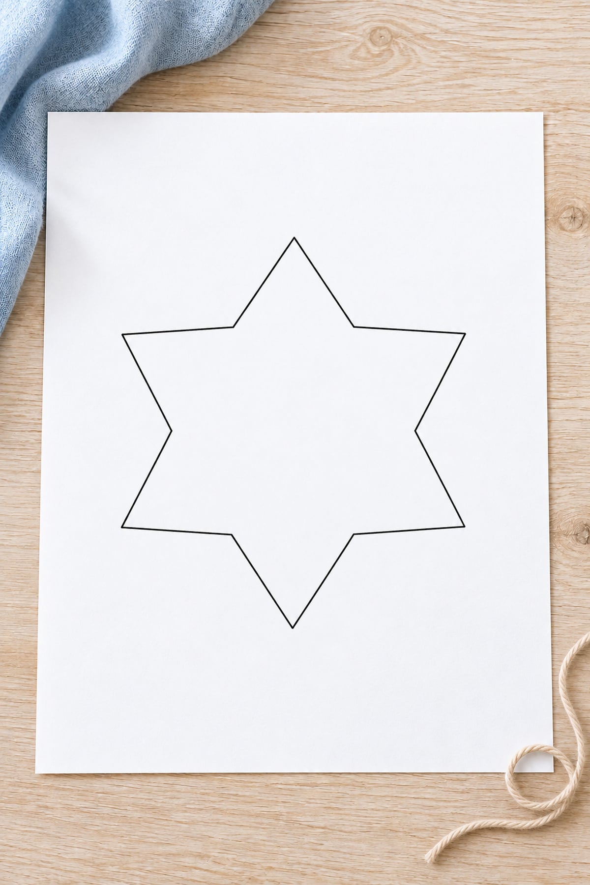 Six-pointed snow star outline on white paper beside a loop of natural cotton twine.