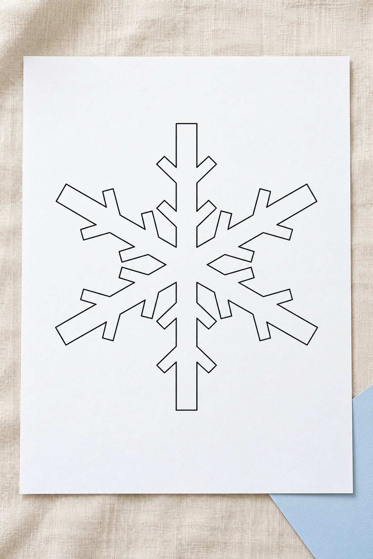 Chevron-branch snowflake outline on white paper over ivory linen, with a pale blue cardstock corner.