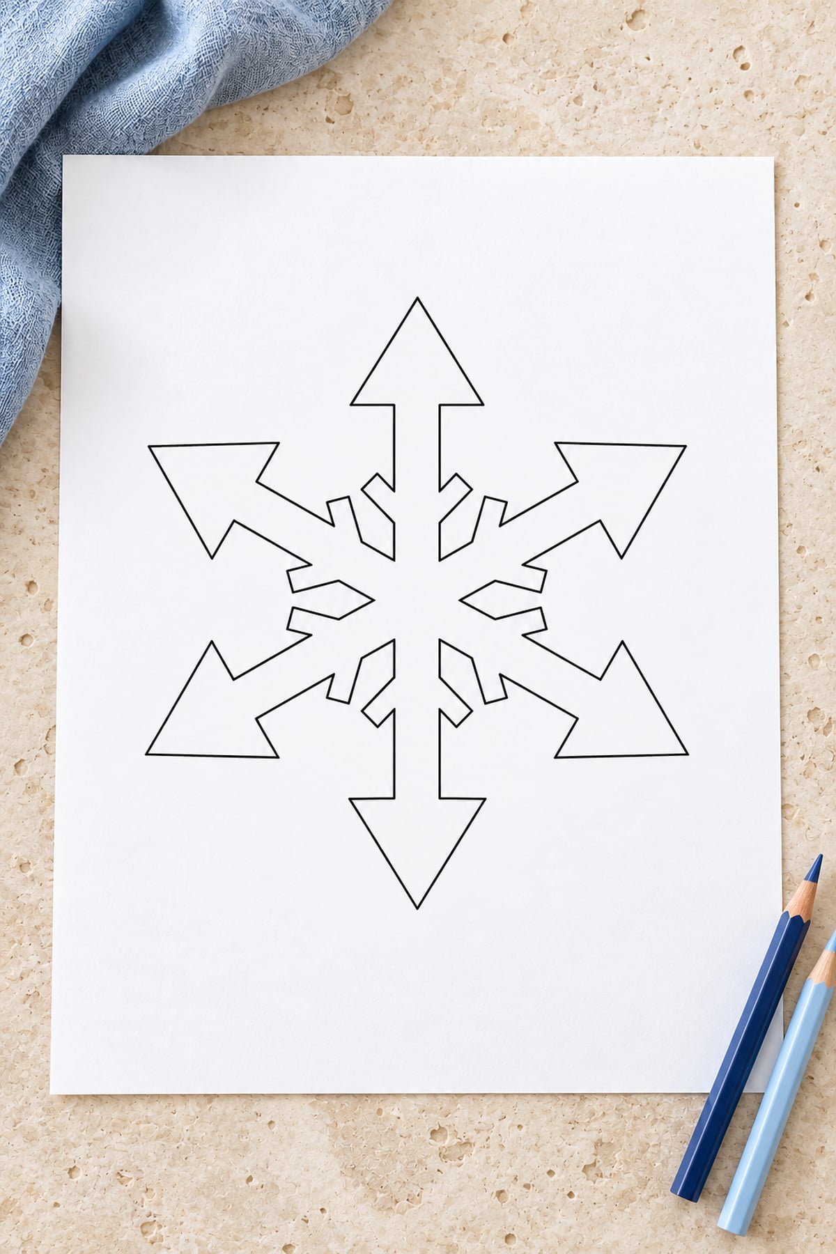 Arrowhead-tip snowflake template on a light limestone surface beside navy and pale blue pencils.