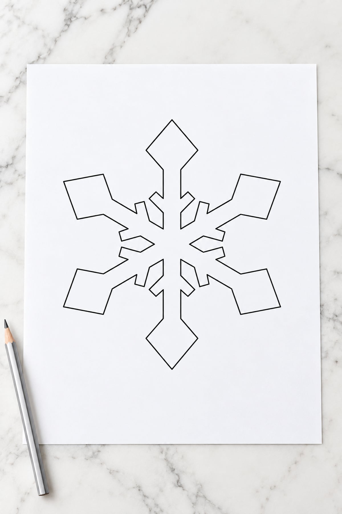 Diamond-tip snowflake template on white marble beside a silver-coloured pencil.