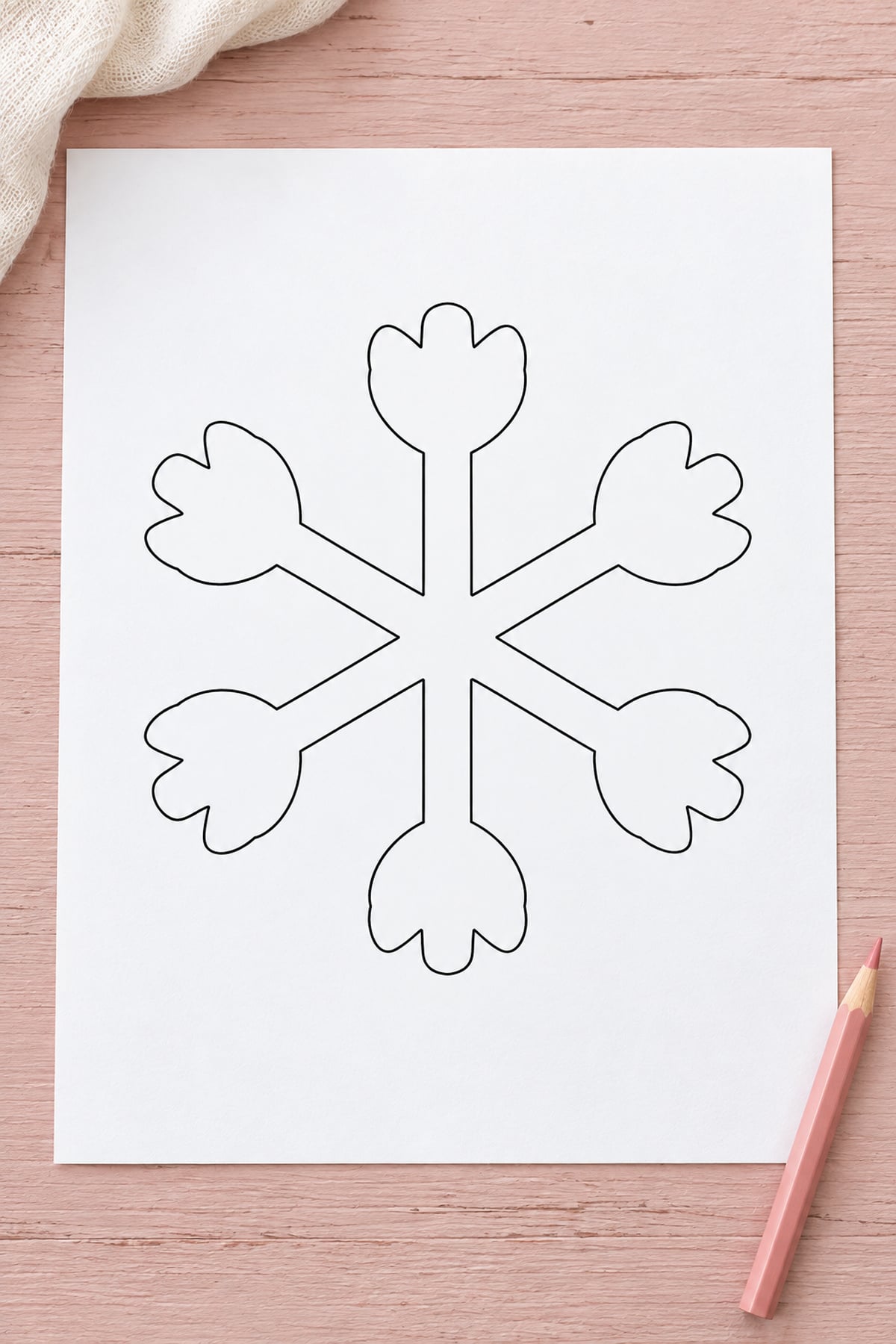 Snowflake outline with tulip-shaped tips on a blush wooden surface beside a pink pencil.