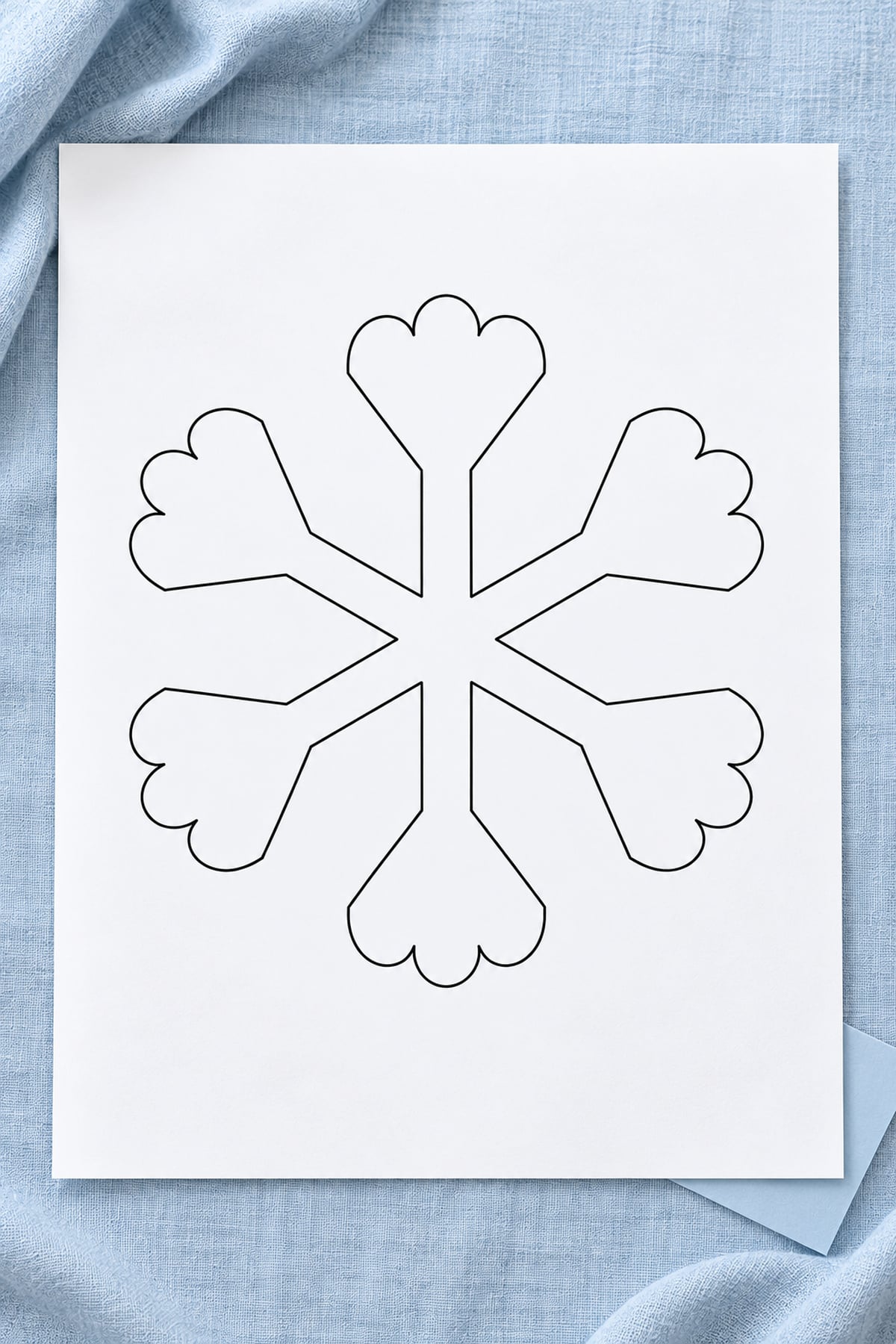 Snowflake template with scalloped fan-shaped tips on white paper over pale blue linen.